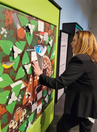 Starkloff Disability Institute Executive Director Lori Becker interacting with a bright green forest display from "i am wild: a charley harper exhibit."