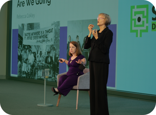 Rebecca Cokely delivery 2024 keynote with ASL interpreter on stage.